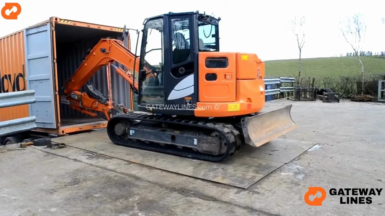 An orange excavator entering an open shipping container